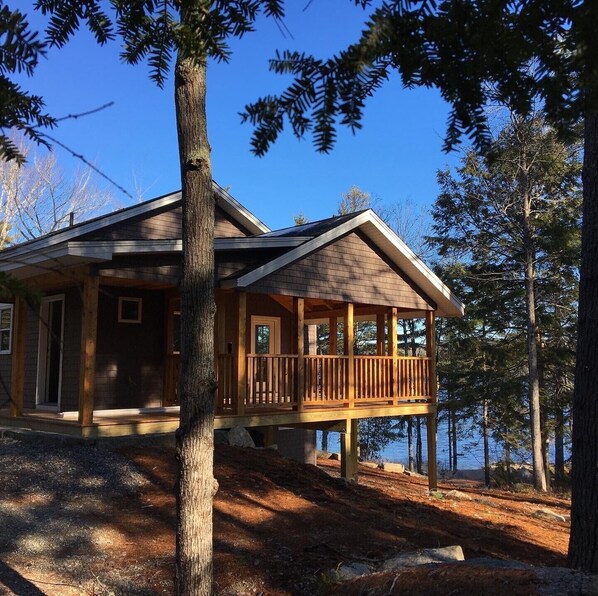 A cabin with a covered porch, wooden exterior, and a view of a lake.