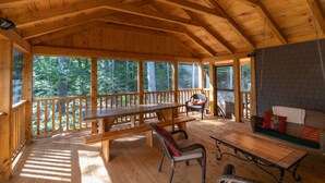 A wooden cabin with a large dining table, benches, and wicker chairs. - Peaceful, family-friendly Maine getaway at newly built scenic lakefront cottage  (Clifton)