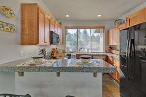 A kitchen with wooden cabinets, a black refrigerator, granite countertops, and a window with blinds.