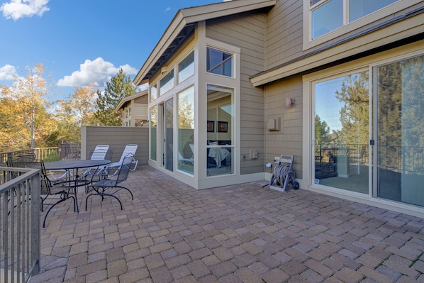 A modern house with a patio area featuring a table and chairs, large windows, and a view of trees.