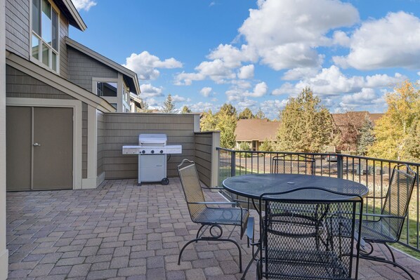 A patio with a grill, a round table, and chairs.