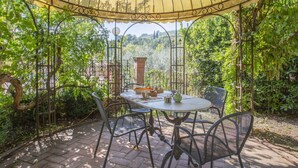 A covered patio area with a table and chairs, surrounded by lush greenery and a view of the countryside. - Cosy apartment for 4 guests with hot tub, WIFI, pool, TV, patio and pets allowed (Montecatini Terme)