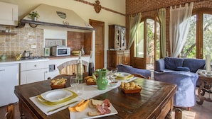 A rustic kitchen with a dining area, featuring a wooden table set for a meal, a blue sofa, and a view of the outdoors through large windows. - Cosy apartment for 4 guests with hot tub, WIFI, pool, TV, patio and pets allowed (Montecatini Terme)