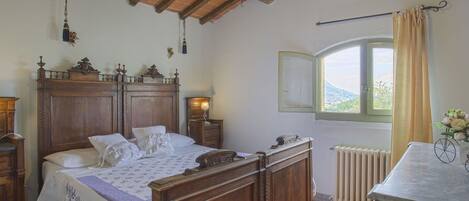 Un dormitorio tradicional con una cama de madera, una mesita de noche, un tocador y una ventana con vistas.