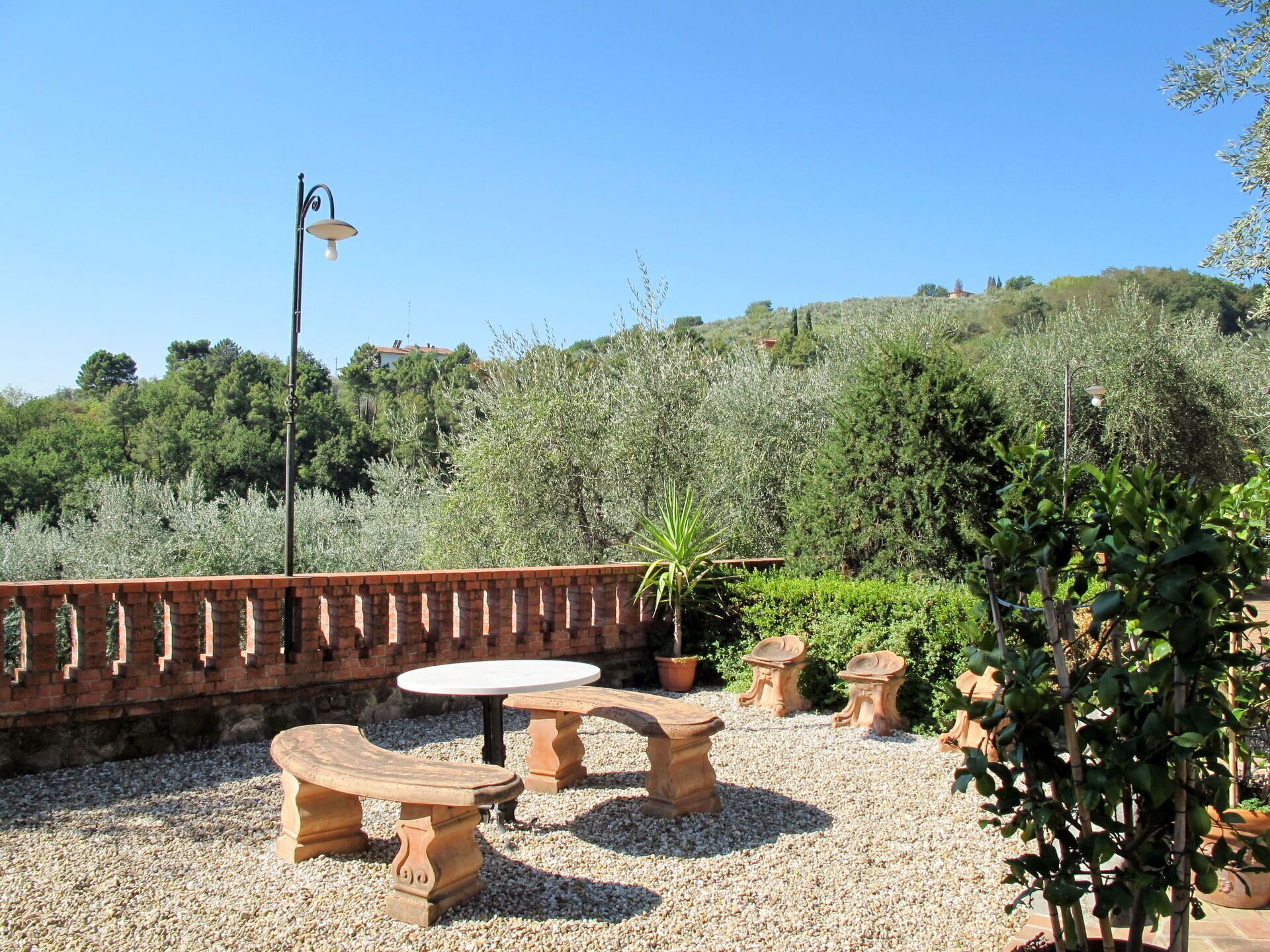 An outdoor patio with stone benches and tables, surrounded by gravel and potted plants.