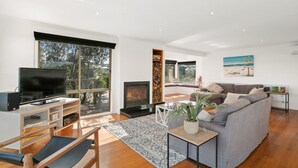 A modern living room with a TV, sofa, and fireplace. - The Deck House - sleeps 8 (SMITHS BEACH)