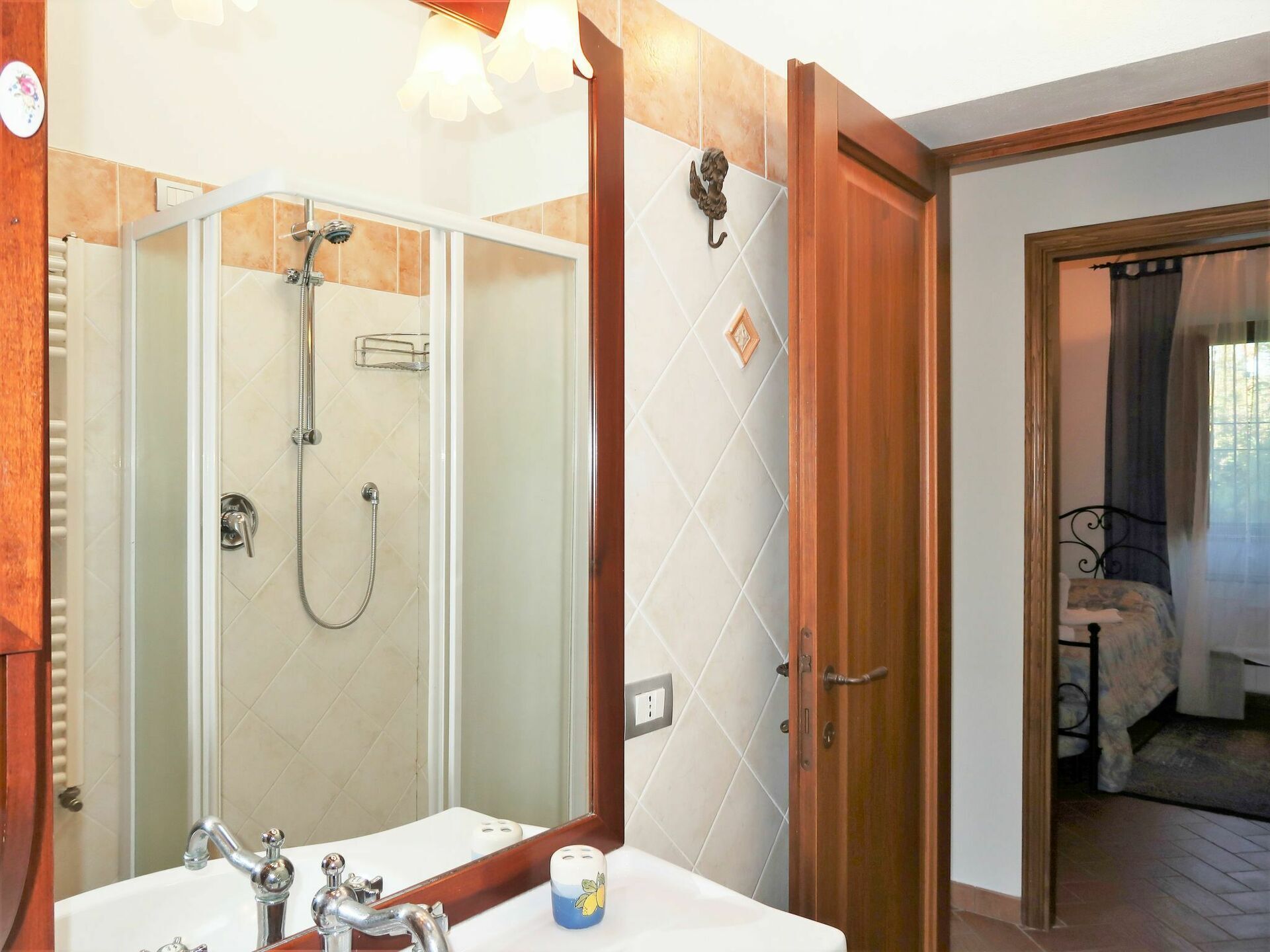 A bathroom with a glass-enclosed shower, a sink with a mirror, and a wooden door leading to a bedroom.