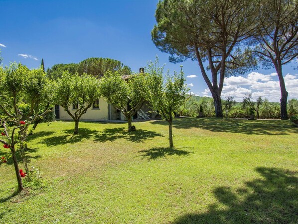 A property with a well-maintained lawn, several trees, and a building with a tiled roof.