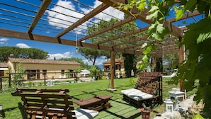 Eine Holzpergola mit einer Bank und Tischen, umgeben von einem üppigen Garten und einem Poolbereich.