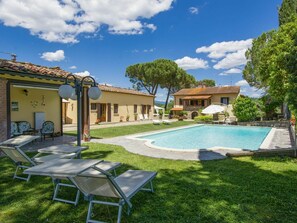 Zona de piscina amb gandules, un petit pati i un edifici amb teulada enrajolada.