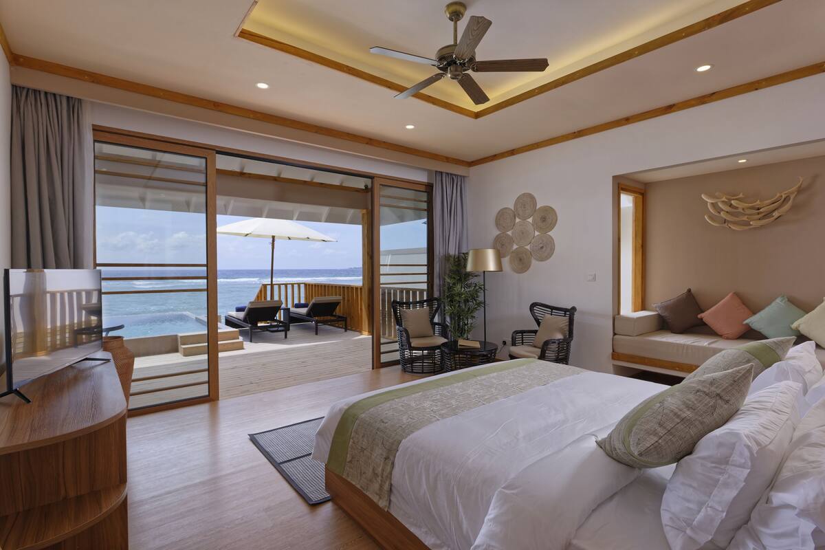A spacious bedroom with a large bed, a desk, and a balcony with a view of the ocean.