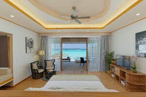 A bedroom with a bed, a television, a ceiling fan, and a view of the ocean.