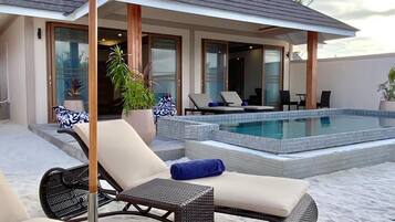 A poolside area with lounge chairs and an umbrella, a pool, and a building with large windows and doors.