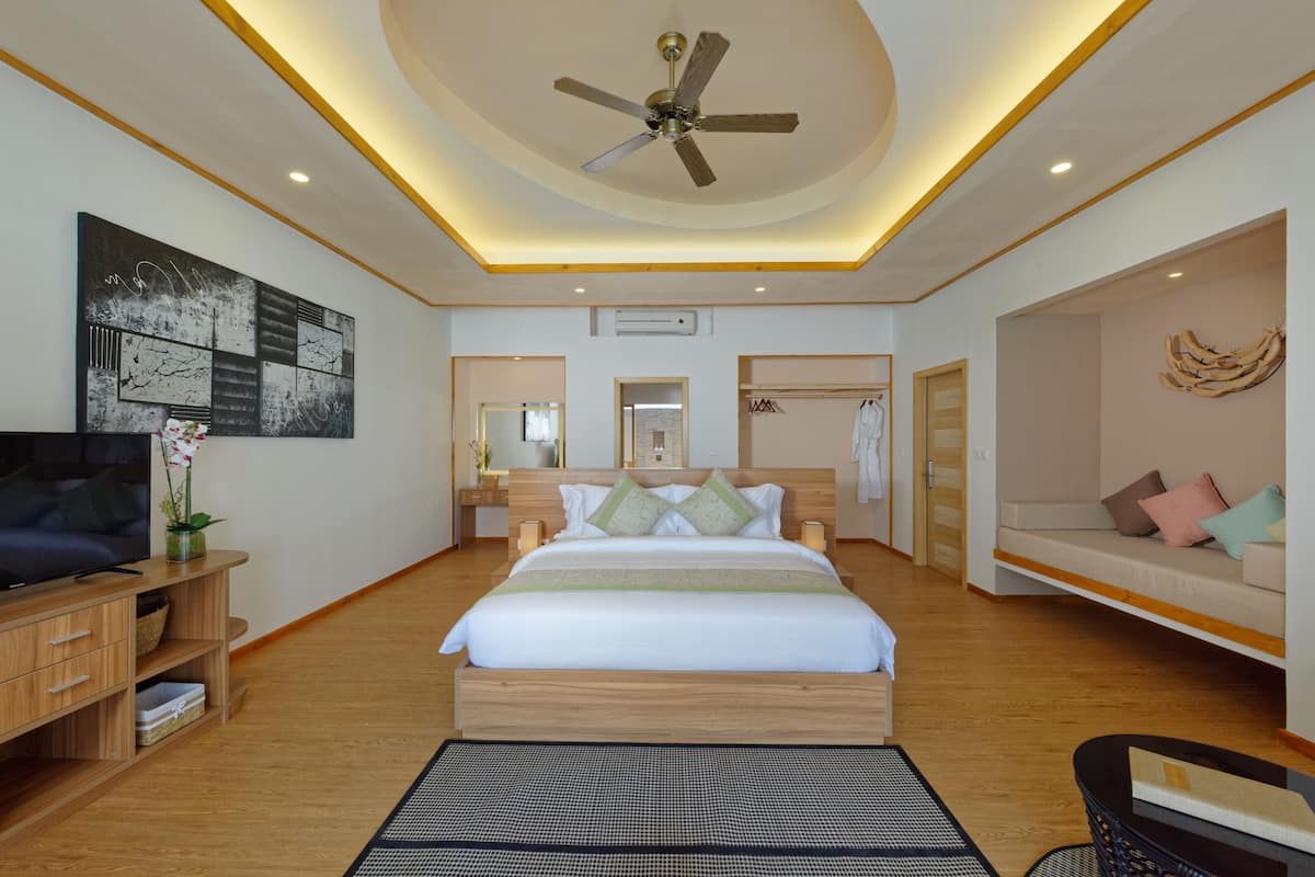 A modern hotel room with a large bed, a ceiling fan, a flat-screen TV, a bedside table, and a sofa.