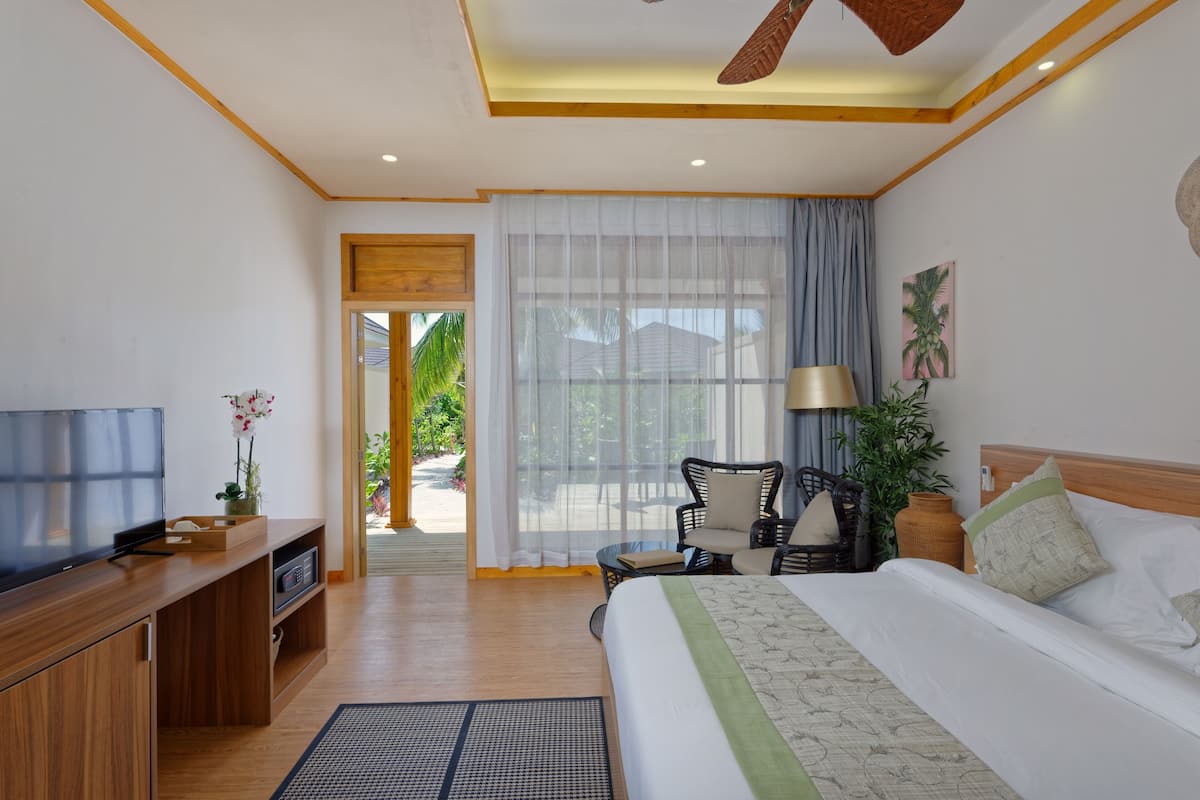 A hotel room with a bed, a TV, a desk, a chair, a lamp, and a view of the outdoors.