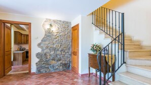 A spacious hallway with a stone accent wall, a kitchen area, and a staircase with a metal railing. - Cosy apartment for 8 people with pool, WIFI, TV, terrace, pets allowed and panoramic view (Pergine Valdarno)