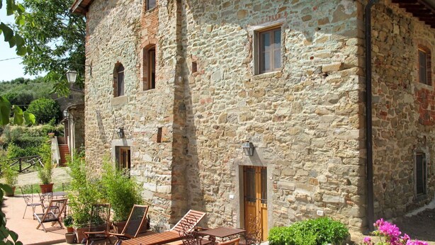 Un bâtiment en pierre, à l’aspect rustique, avec une porte en bois et un petit jardin agrémenté de mobilier d’extérieur.