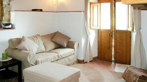 Un salon chaleureux avec un canapé beige, une petite table, un banc rembourré et une porte en bois.