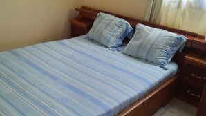 A bed with a striped blue and white bedspread, two matching pillows, wooden headboard, and a wooden nightstand with drawers. - Nzecy Appart. A studio with a velvety, air-conditioned living room. (Libreville)