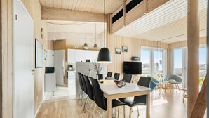 A modern kitchen with wooden paneling, a dining area with a white table and black chairs, and large windows offering a view of the city. - Pet friendly home in Faaborg with sauna (Faaborg)
