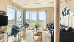 A modern living room with a large window, a black leather sofa, a wooden coffee table, and a TV on a stand. - Pet friendly home in Faaborg with sauna (Faaborg)