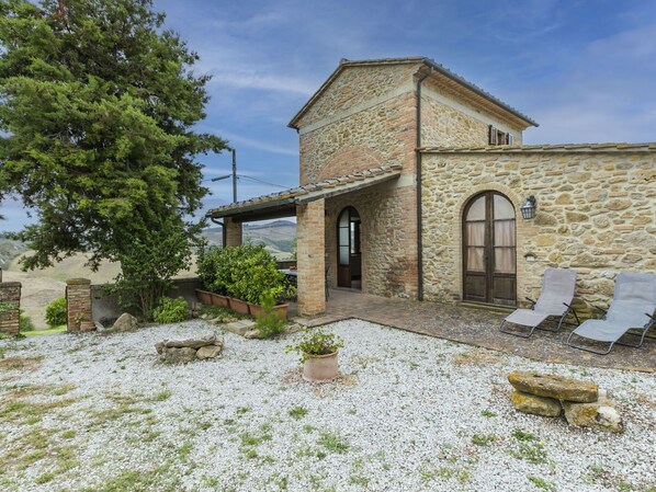 A stone building with a covered patio, outdoor seating, and a view of the hills.