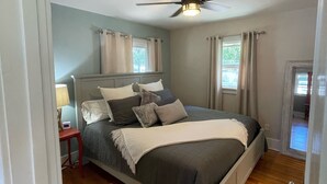 Une chambre Ă coucher avec un lit, un ventilateur de plafond, une table de chevet, une lampe et une vue sur lâextĂ©rieur.