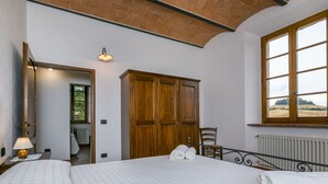 Une chambre avec un grand lit, une armoire en bois, une fenêtre donnant sur un beau paysage et un radiateur.