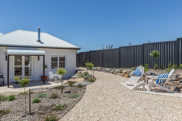 A modern house with a gravel driveway, outdoor seating area with Adirondack chairs, and a fenced backyard.