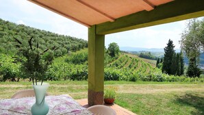 Une table d’extérieur, agrémentée d’un vase et d’une nappe, placée devant un paysage de vignes et de collines.