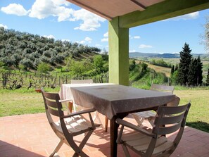 An outdoor dining area with a table and chairs, overlooking a vineyard and rolling hills.