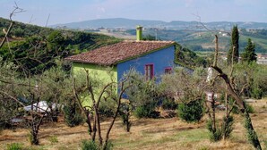 A small, single-story building with a tiled roof, surrounded by trees and hills in the background.
