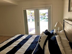 Une chambre d’hôtel avec un lit, une table de chevet, une lampe et une vue sur un port de plaisance, visible à travers la porte.