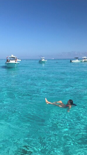 Klares, blaues Meer mit Booten und einer schwimmenden Person.