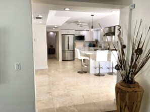 Une cuisine moderne avec des meubles blancs, des appareils en acier inoxydable et un îlot central doté de tabourets de bar.
