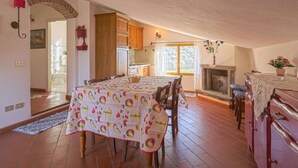 Un'accogliente zona pranzo con tavolo imbandito per quattro persone, un caminetto e una cucina sullo sfondo.