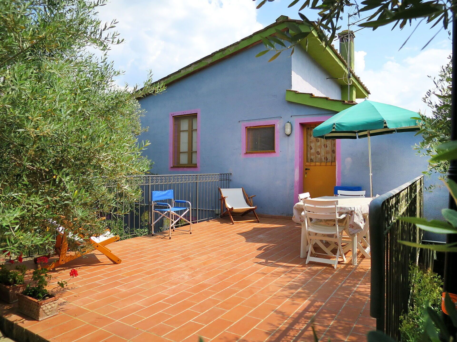 A patio with a table and chairs, a small garden, and a building with a blue and pink facade.