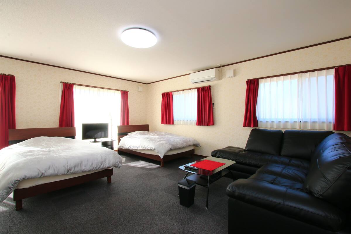 A hotel room with two beds, a black leather sofa, a small table, and a TV.