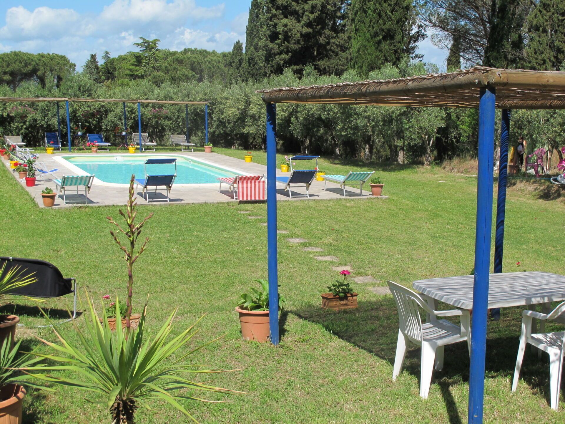 Ein Garten mit Swimmingpool, Liegestühlen und einem Tisch unter einer Pergola.