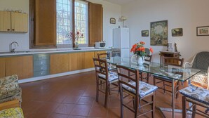 Una cucina con mobili in legno, un tavolo da pranzo con sedie, un frigorifero e una finestra con tende.