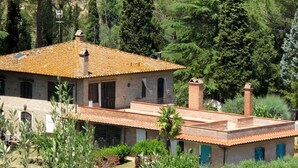 Una villa rustica con tetto in tegole, circondata da uliveti e vegetazione lussureggiante.