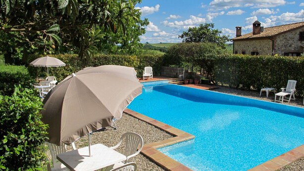 Una piscina con agua azul cristalina, rodeada de sillas y sombrillas blancas, y un edificio de piedra al fondo.