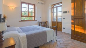Un dormitorio con cama, mesita de noche, lámpara, ventana y puerta.