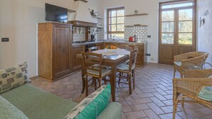 A kitchen with wooden cabinets, a dining table, wicker chairs, and a television. - Beautiful apartment in villa with WIFI, A/C, pool, TV, patio, pets allowed and panoramic view (Castellina In Chianti)