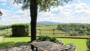 Un tavolo in legno con sedie in metallo in un giardino con vista sui vigneti e sulle colline.