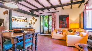Una sala de estar acogedora con sofá y televisor, un comedor con mesa y sillas, y una cocina con ollas colgando.