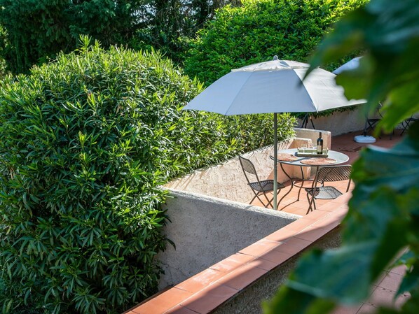 An outdoor patio area with a round table and chairs, a large umbrella, and a bottle of wine.
