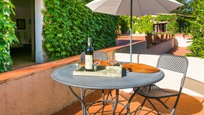 A patio with a table and chairs, a wine bottle, and an umbrella. - Cosy apartment in villa for 2 guests with pool, WIFI, TV and terrace (Colle Di Val D'elsa)