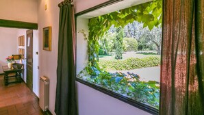 A hallway with a window covered in green ivy, a radiator, a door, and a table with a basket and flowers. - Nice apartment in villa for 4 guests with WIFI, pool, TV, terrace and panoramic view (Colle Di Val D'elsa)