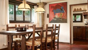 A dining area with a wooden table and chairs, a window with curtains, and a kitchen visible through an open door.